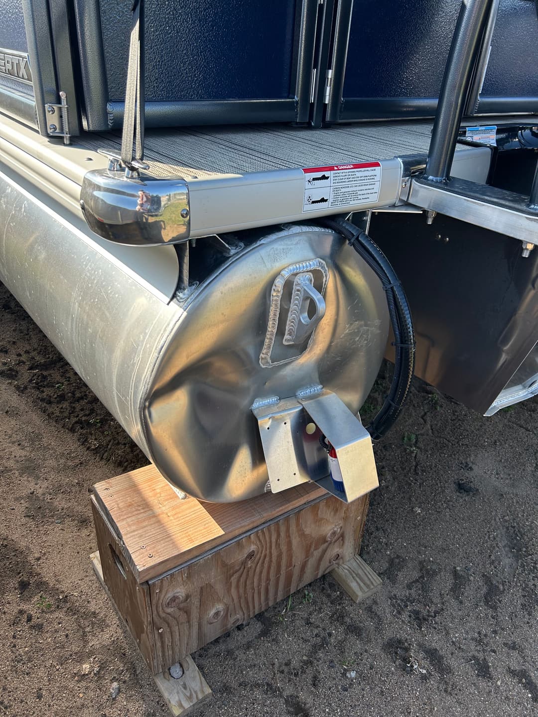 Pontoon boat fuel tank with mounting brackets, positioned on a wooden platform.