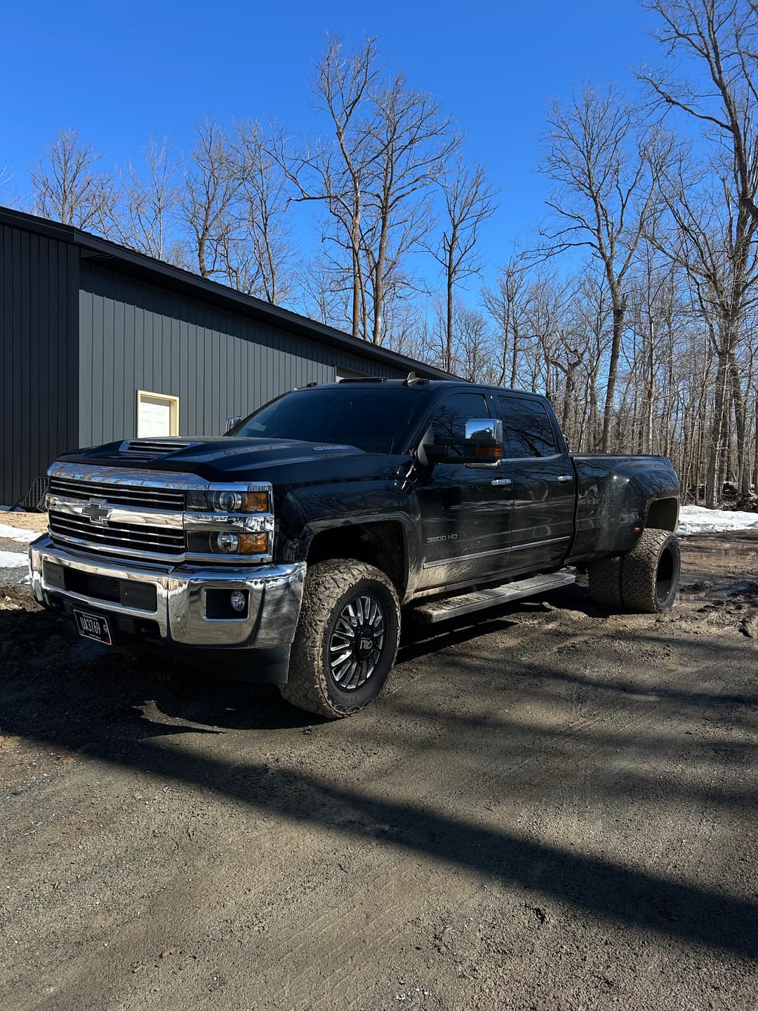 Black Chevrolet Silverado truck parked in front of a gray building in a wooded area.