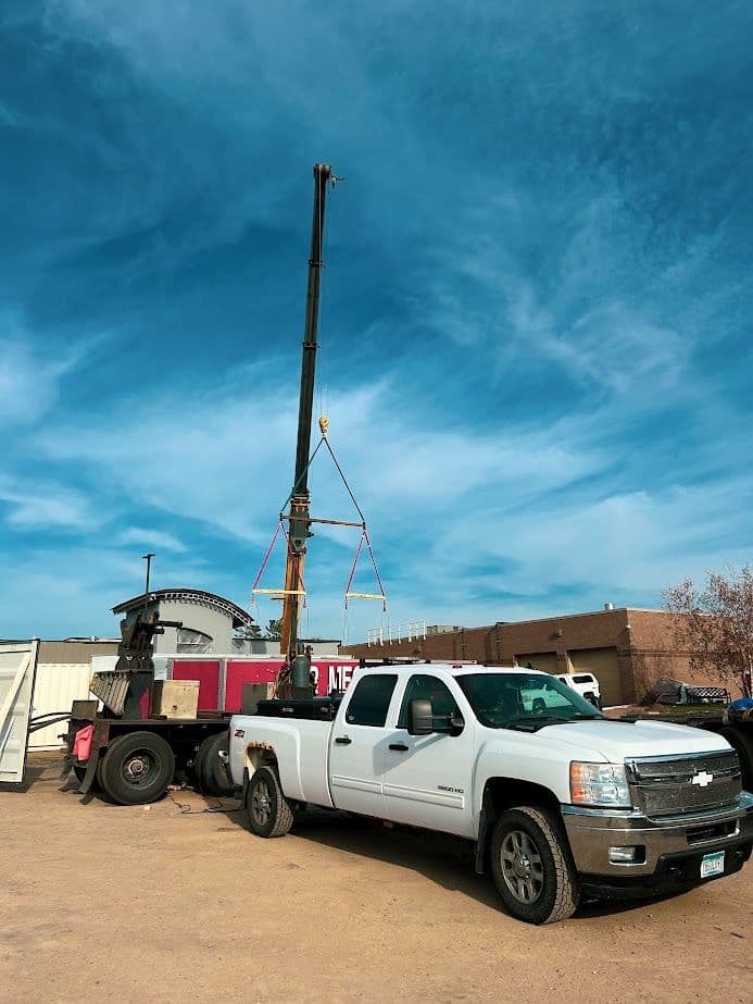 White pickup truck parked near a crane and construction equipment under a blue sky.
