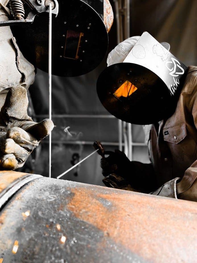 Welder working on metal pipe, sparks flying, with protective gear and focused concentration.