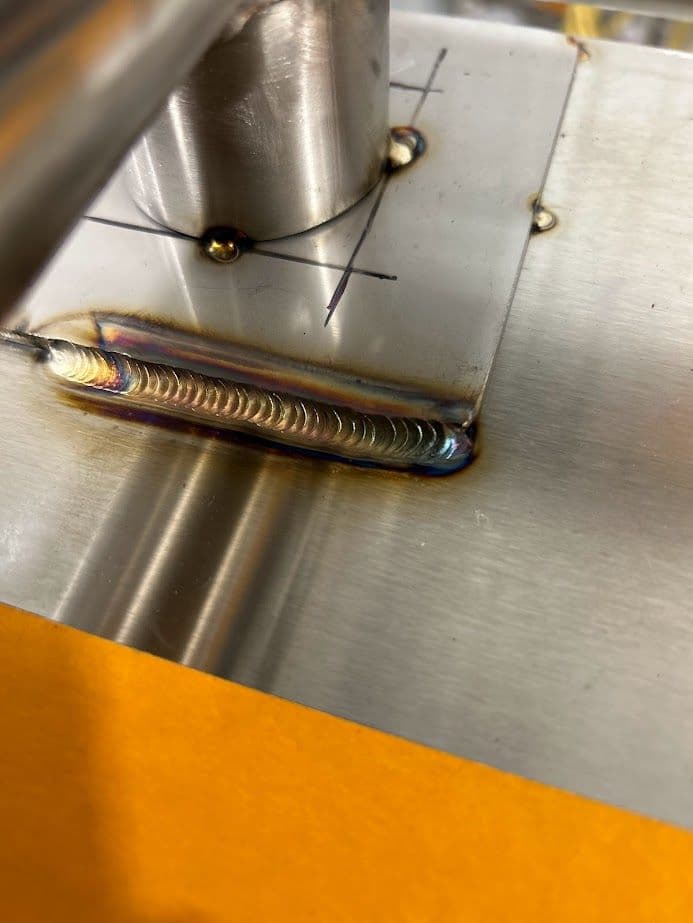 Close-up of a metal weld with colorful heat markings on stainless steel surface.