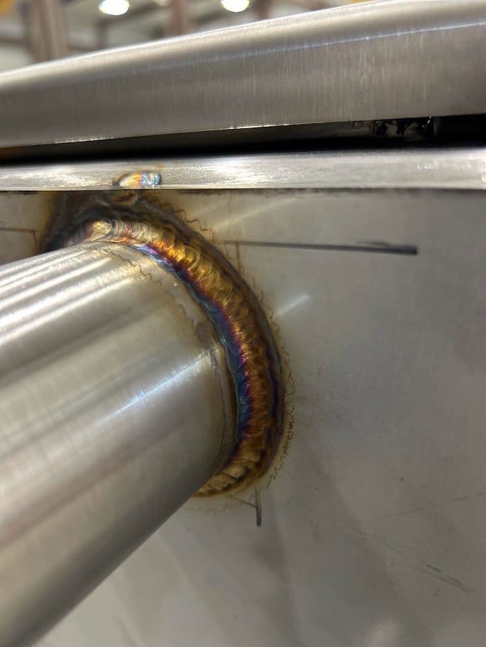 Close-up of a metal weld on a stainless steel surface, showcasing colorful bead patterns.