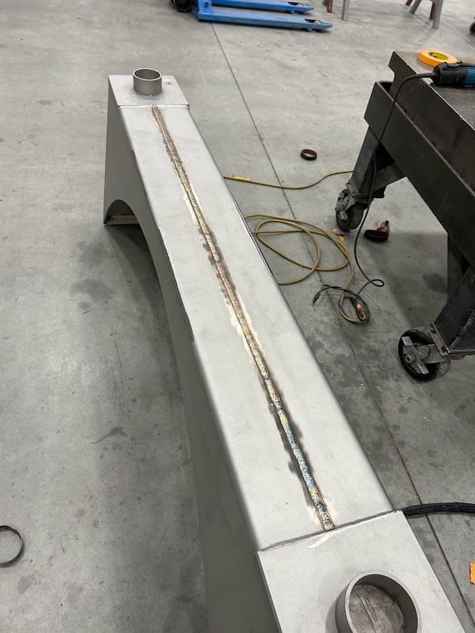 Welded metal beam on workshop floor with visible joint details and tools nearby.
