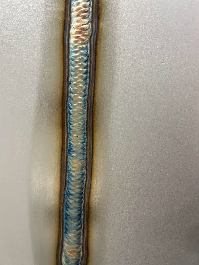 Welding seam detail showing distinct colors and textures on a metallic surface.