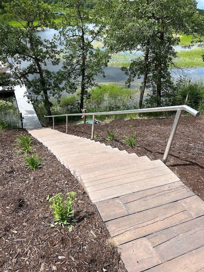 Wooden staircase leading down to a tranquil water body surrounded by trees and greenery.