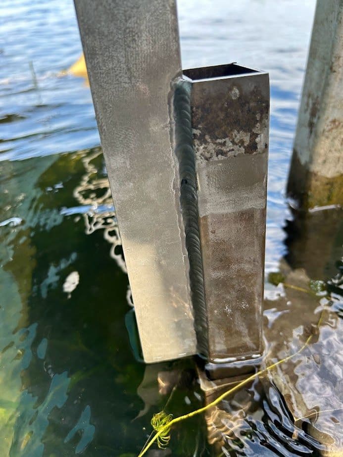 Metal post partially submerged in water with visible welding seam and reflections.