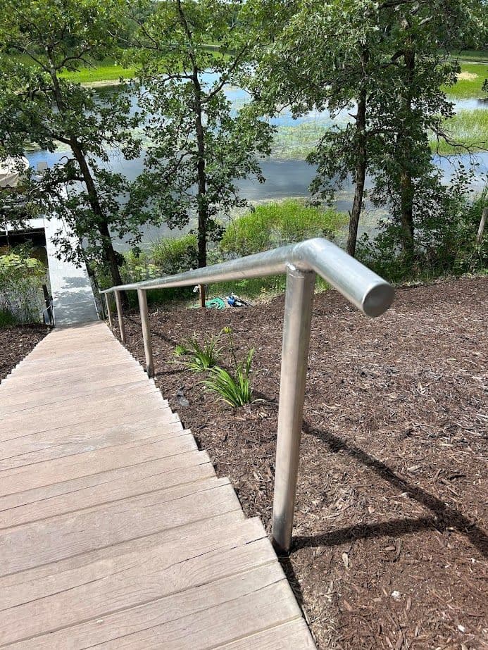 Handrail on wooden staircase leading down to a serene lake surrounded by trees.