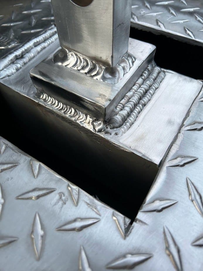 Close-up of welded metal structure with diamond plate texture and intricate weld seams.