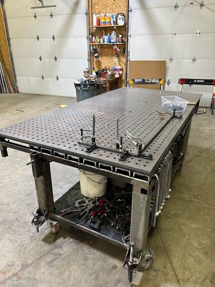 Industrial welding table with adjustable clamps and tools in a workshop setting.