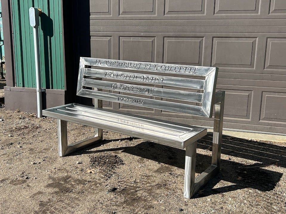 Stainless steel memorial bench engraved with "In Memory of Dan Collett 1972-2018."