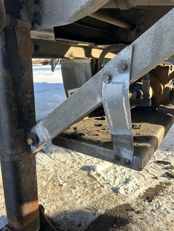 Metal support bracket with weld on machinery, positioned on snowy ground under a truck.