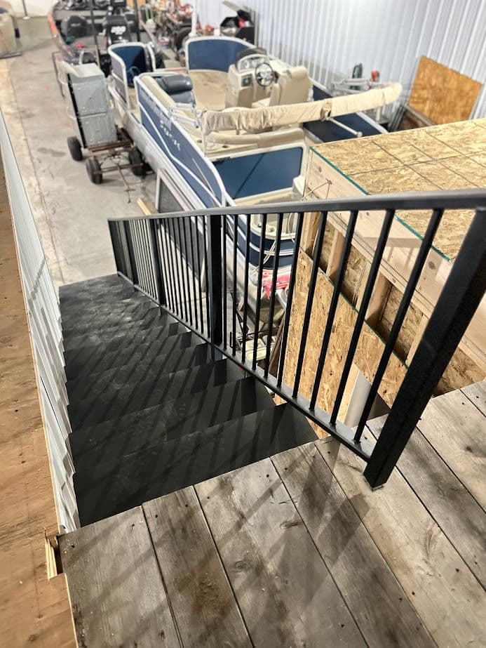 Black staircase leading down to a storage area with boats and equipment in the background.