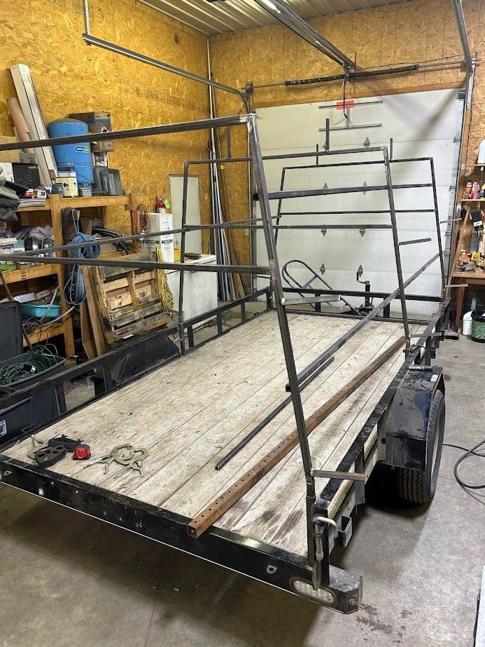 Metal trailer frame in a workshop with wooden floor and tools scattered around.