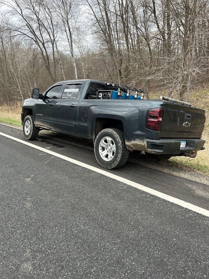 Gray Chevrolet truck parked on a rural road, surrounded by trees and dirt.
