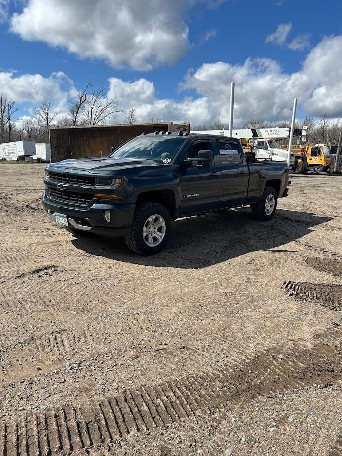 Blue Chevrolet Silverado truck parked on a gravel lot under a cloudy sky.