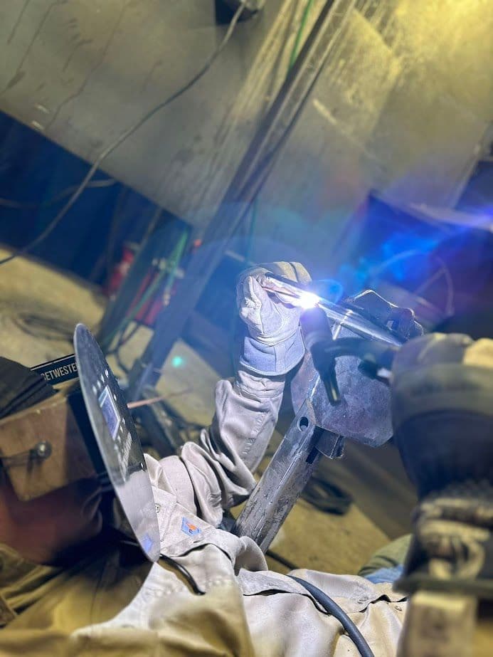 Welder in protective gear using a welding torch in an industrial setting.