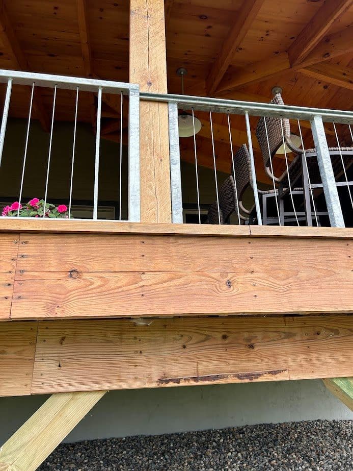 Wooden porch with metal railing and hanging lights, featuring potted flowers below.