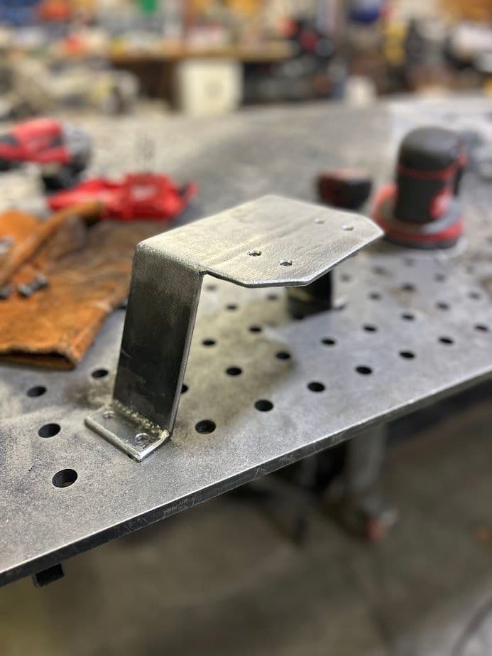 Metal bracket on a workbench, surrounded by tools and equipment in a workshop setting.