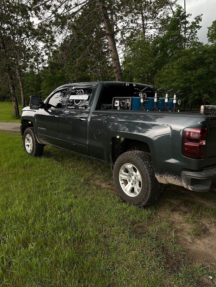 Gray pickup truck parked on a grassy path surrounded by trees, equipped for outdoor activities.