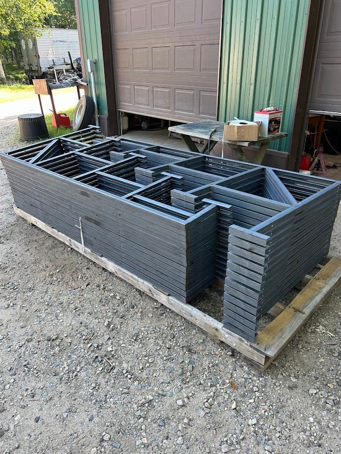 Stacked metal pallets arranged neatly on a gravel surface near a storage building.