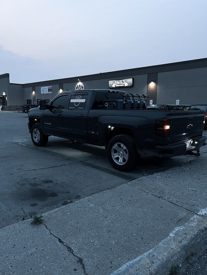 Black Chevrolet truck parked near commercial building at dusk, showcasing its cargo rack and tires.