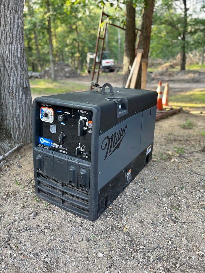 Miller portable generator on gravel in a wooded area, ideal for outdoor power needs.