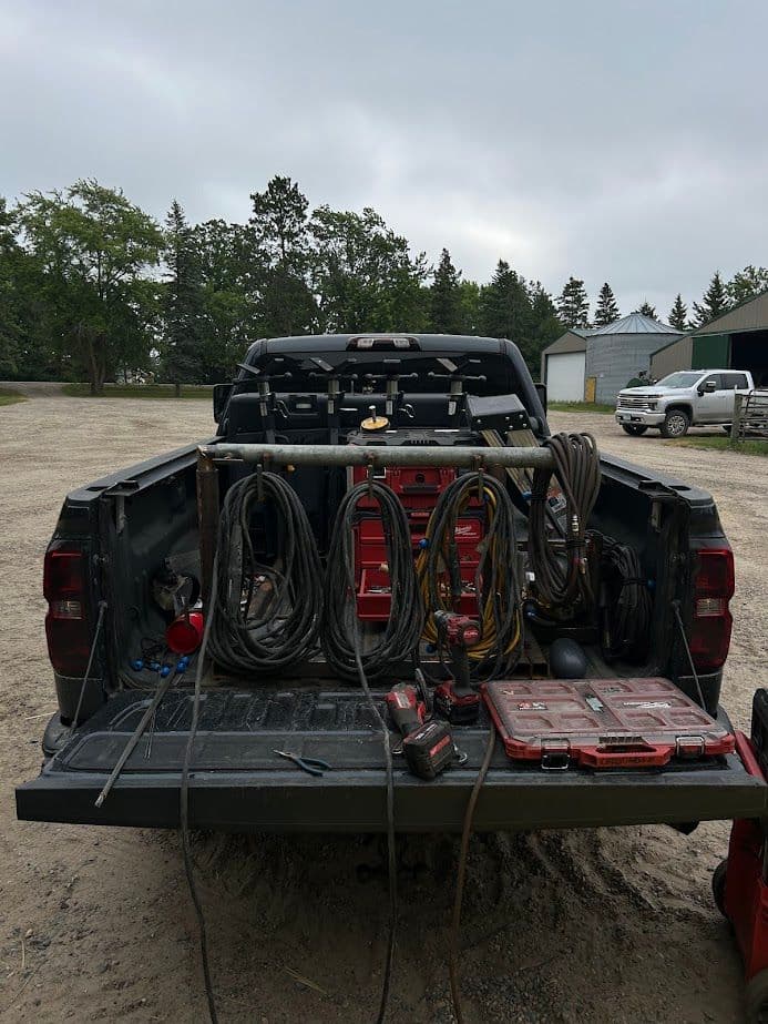 Back of a pickup truck loaded with tools, cords, and equipment on a construction site.