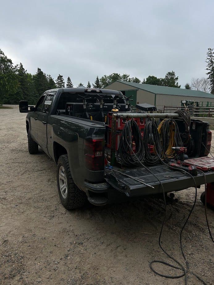 Pickup truck with tools and equipment in the bed, parked in a gravel area near a building.