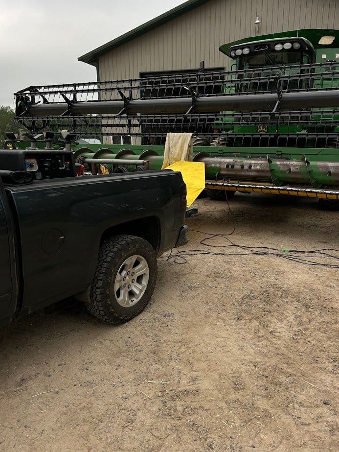Pickup truck parked near a green combine harvester in a farmyard setting.