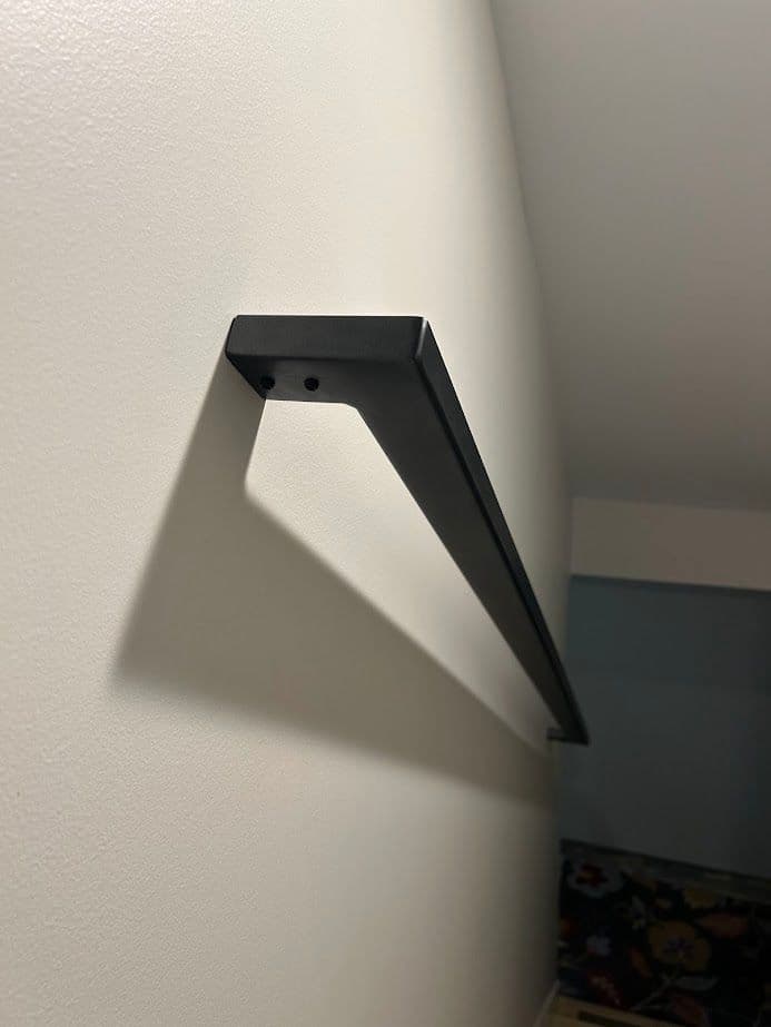Black wall-mounted shelf bracket casting a shadow on a white wall.