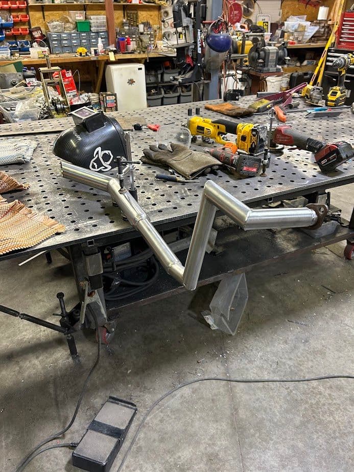 Metal exhaust pipe prototype on a workbench surrounded by tools and equipment in a workshop.