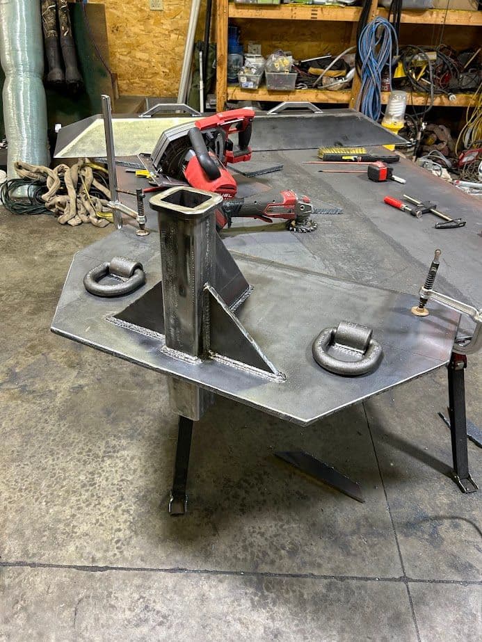 Metal fabrication stand with welded joints and cable attachments in a workshop setting.