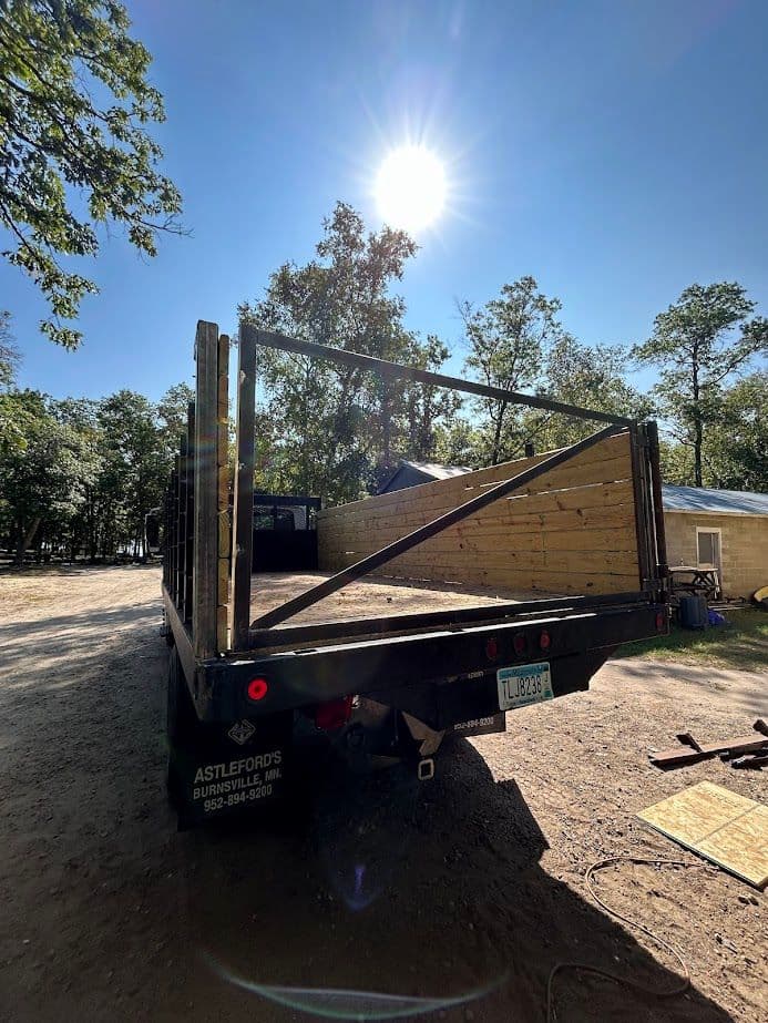 Flatbed truck with wooden frame against a bright sun and wooded area. Ideal for transportation.