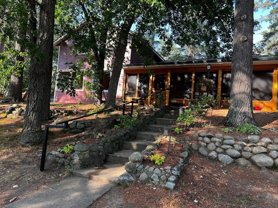 Charming cabin surrounded by trees with a stone pathway and welcoming porch.