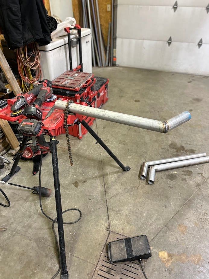 Pipe bending tool setup in a workshop with tools and equipment in the background.