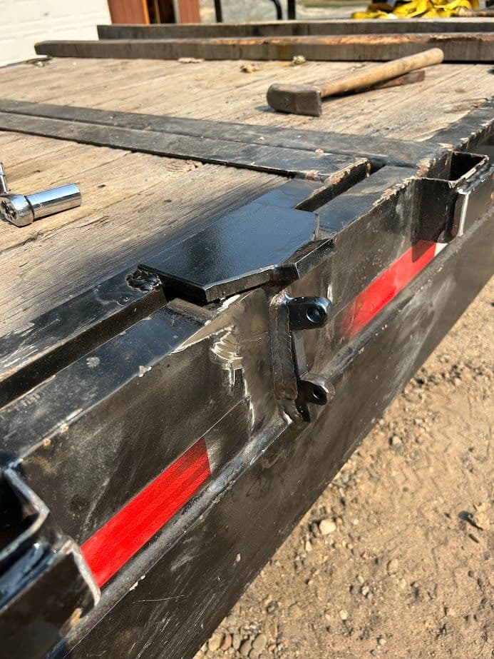 Close-up of a damaged trailer hitch with tools and wooden planks in the background.