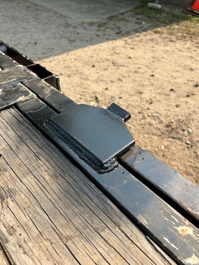Black metal latch on wooden surface in outdoor setting, showcasing craftsmanship and detail.