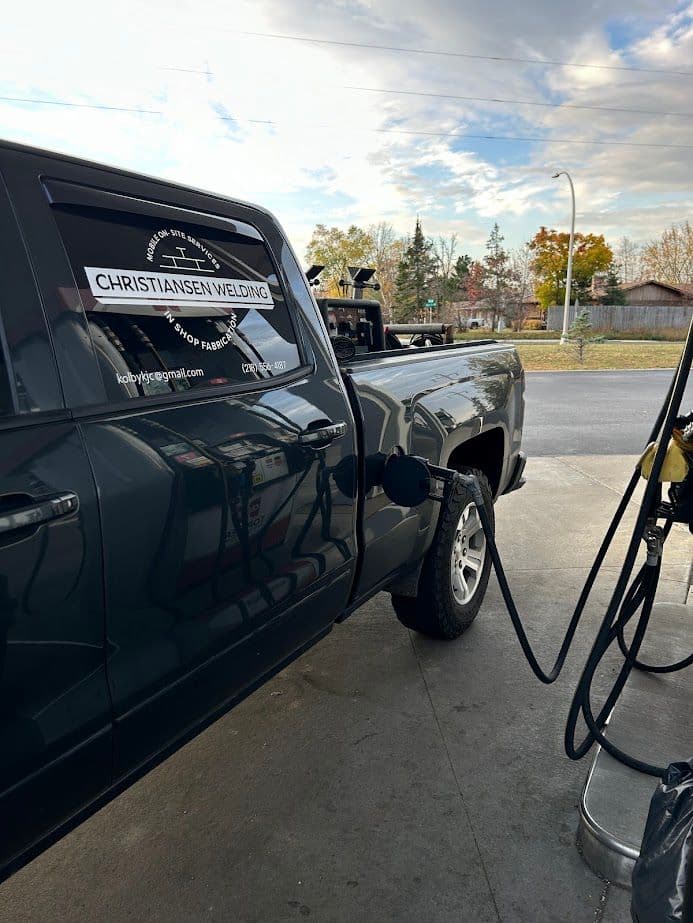 Pickup truck being fueled at a gas station with a welding business logo on the side.