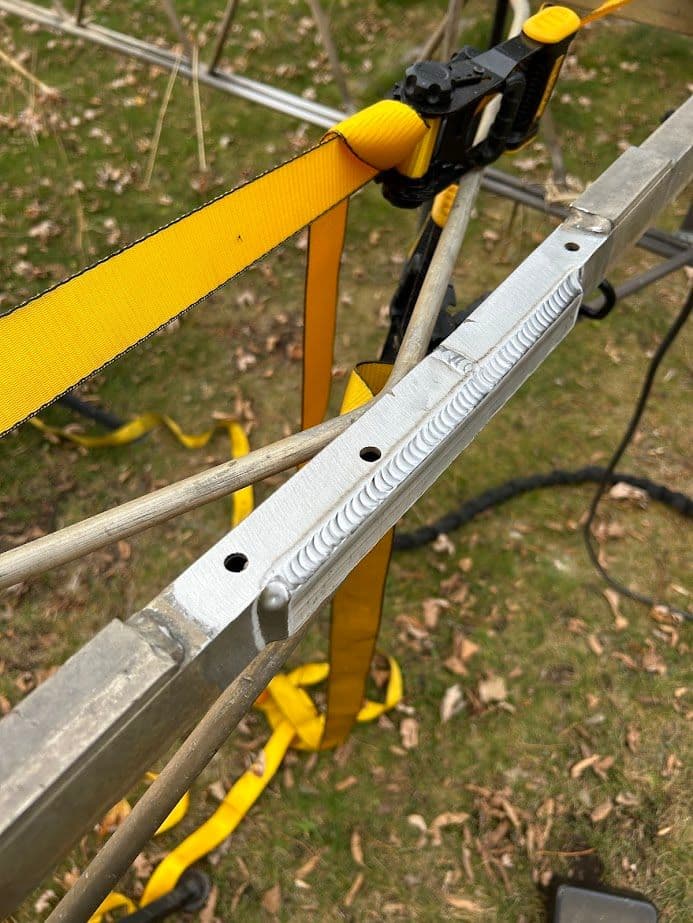 Close-up of aluminum frame with welding detail and yellow straps on grass background.
