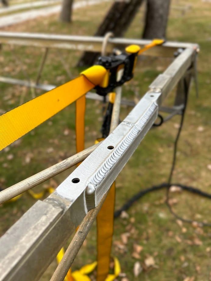 Aluminum frame with yellow straps, set in a grassy outdoor area, highlighting secure fastening.