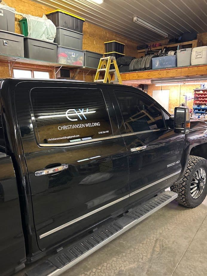 Black pickup truck with Christian Welding logo parked in a workshop with tools and equipment.