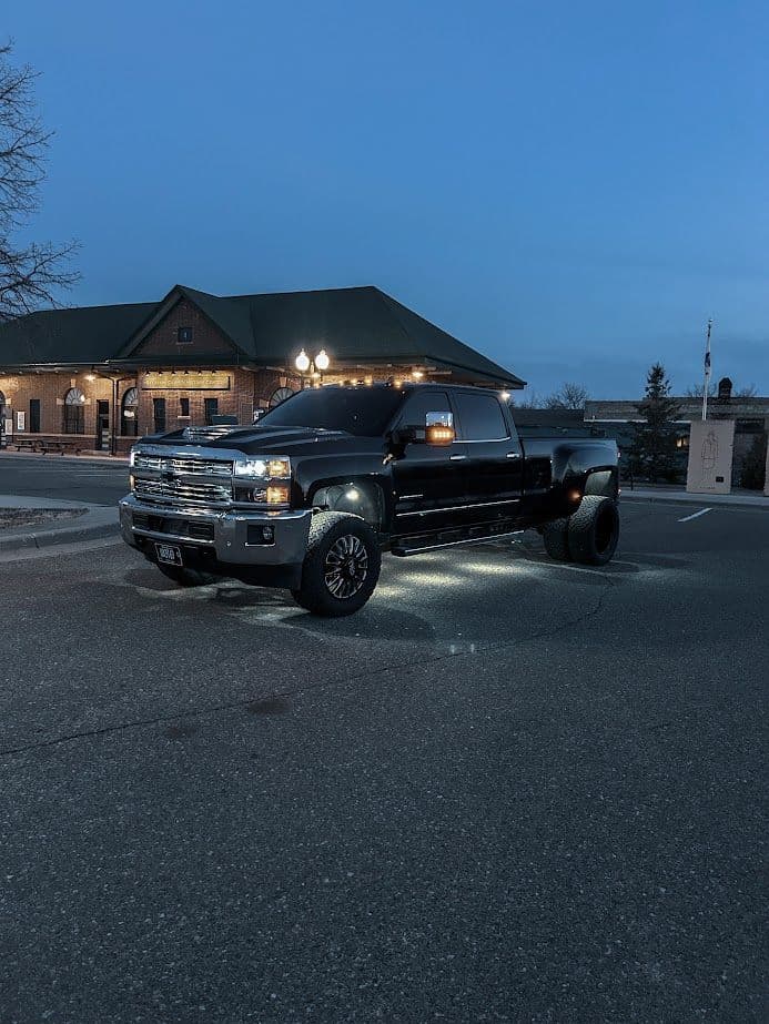 Black lifted truck parked in front of a rustic building at dusk with illuminated features.