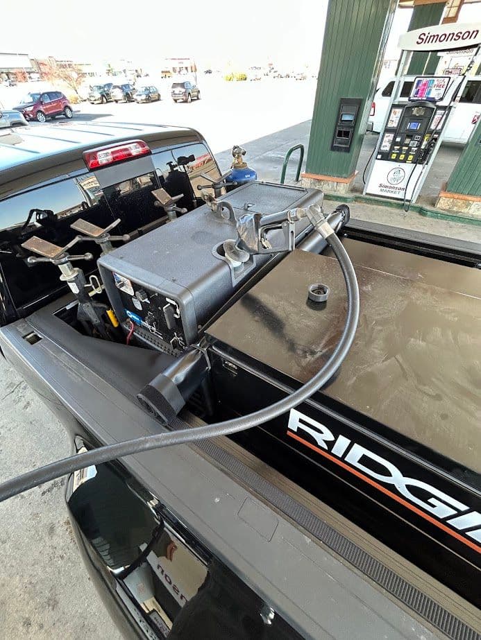 Fuel transfer pump equipment mounted in truck bed at gas station, ready for use.