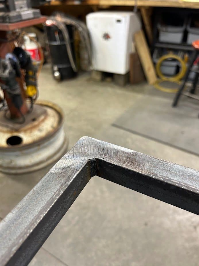 Close-up of a metal weld joint with a workshop background featuring tools and equipment.
