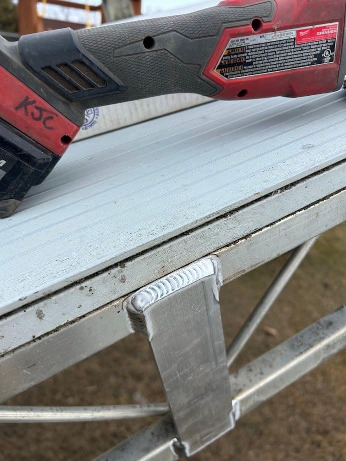 Cordless power tool on aluminum ladder, highlighting tool grip and attached safety features.