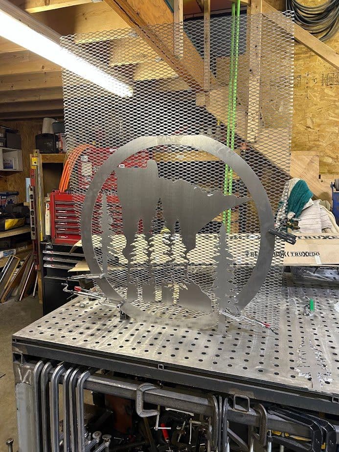 Metal art sculpture of trees and mountains on a workshop table, showcasing craftsmanship.