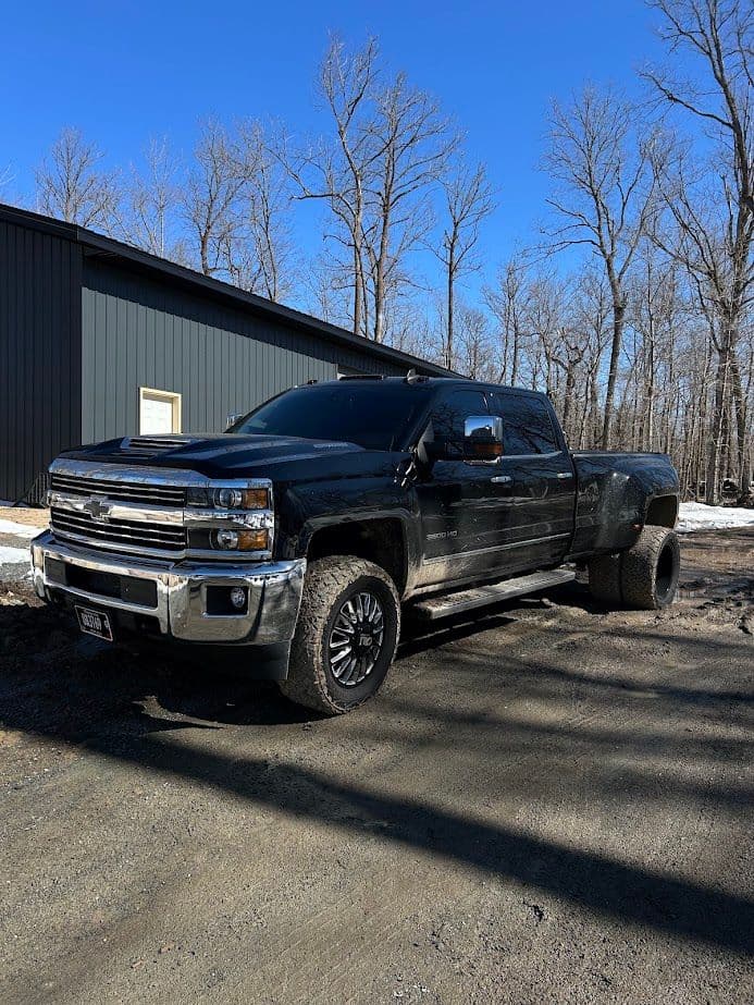 Black Chevrolet Silverado truck parked in a wooded area with a clear blue sky.