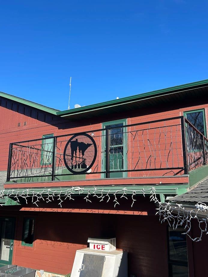 Red building with balcony featuring metal tree design and holiday lights under blue sky.