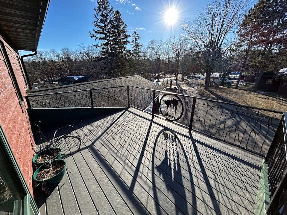 Sunny balcony view with metal railing, potted plants, and surrounding trees.
