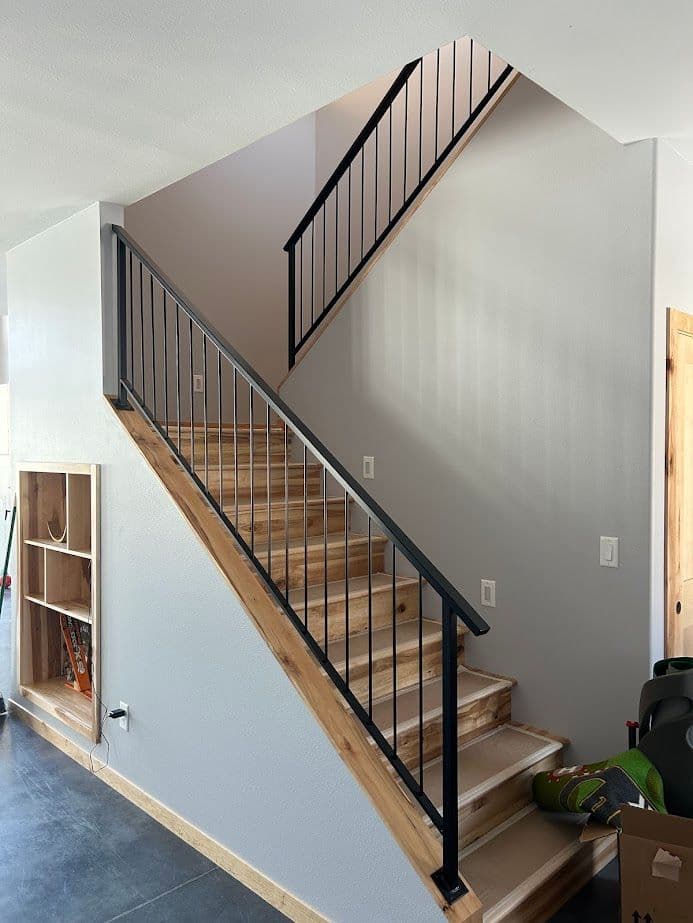 Modern staircase with wooden steps and black metal railing in a bright entryway.